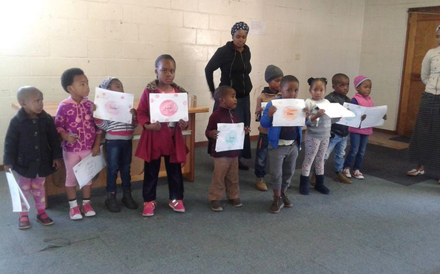 Children in an Early Learning Centre classroom in South Africa holding up their work.