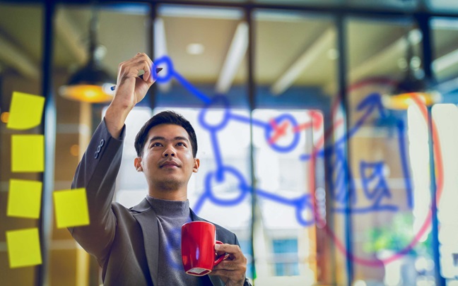 Businessman holding coffee mug and writing data on transparent board