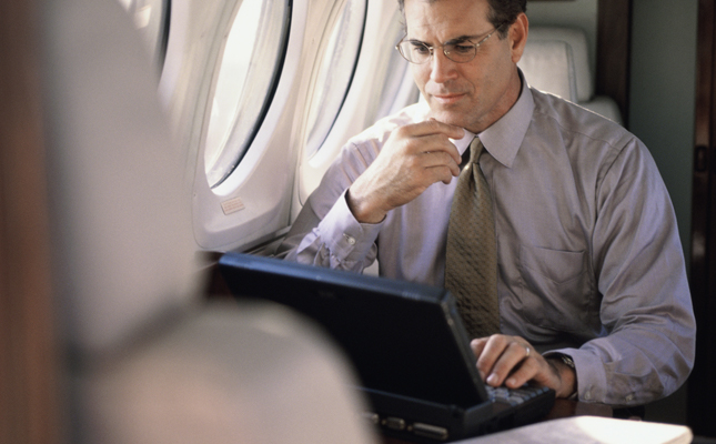 Man sitting in the window seat of an airplane looking at a laptop