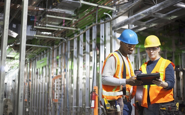 Two construction workers on a job site looking at a tablet
