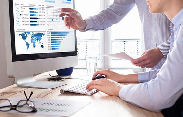 Man sitting at computer with another man's hand pointing to the screen